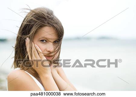 Teenage girl with hair blowing across her face, hands covering ears, looking at camera View Large Photo Image Stock Photo - Teenage girl with hair blowing across her face, hands covering ears, looking at camera. Fotosearch