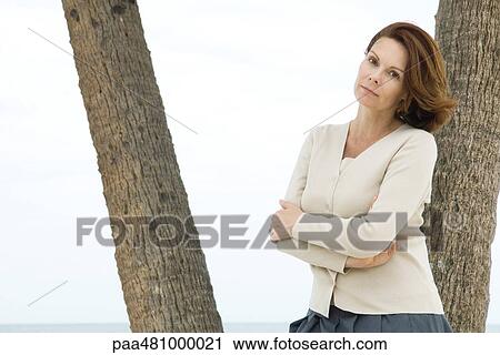 Woman leaning against tree trunk, arms folded, looking at camera View Large Photo Image Stock Image - Woman leaning against tree trunk, arms folded, looking at camera. Fotosearch