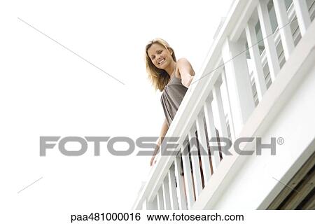 Woman standing on balcony, smiling at camera, low angle view View Large Photo Image Stock Photograph - Woman standing on balcony, smiling at camera, low angle view. Fotosearch