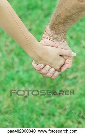 Stock Image - Couple holding hands outdoors, cropped view. Fotosearch