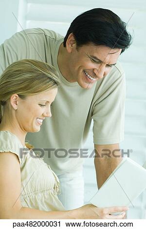 Stock Image - Couple reading book together, both smiling, close-up. Fotosearch