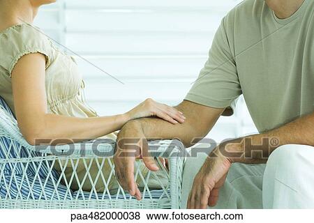 Stock Photo - Couple sitting together, woman touching man's arm, cropped view. Fotosearch