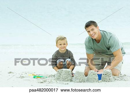 Father and son building sand castle together, both smiling at camera View Large Photo Image Stock Photo - Father and son building sand castle together, both smiling at camera. Fotosearch
