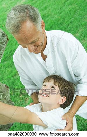 Stock Image - Grandfather and grandson outdoors together, smiling at each other, tilted high angle view. Fotosearch