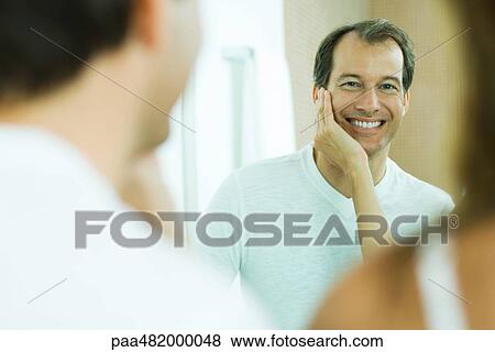 Man with wife's hand on his cheek, smiling at reflection in mirror, over the shoulder view View Large Photo Image Stock Photo - Man with wife's hand on his cheek, smiling at reflection in mirror, over the shoulder view. Fotosearch