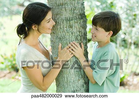 Mother and son leaning against tree trunk, smiling at each other, side view View Large Photo Image Stock Photo - Mother and son leaning against tree trunk, smiling at each other, side view. Fotosearch