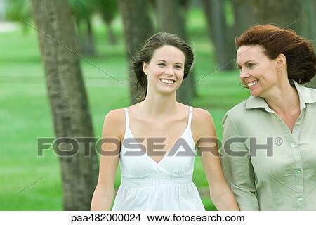 Mother and teenage daughter walking together outdoors, both smiling View Large Photo Image Picture - Mother and teenage daughter walking together outdoors, both smiling. Fotosearch