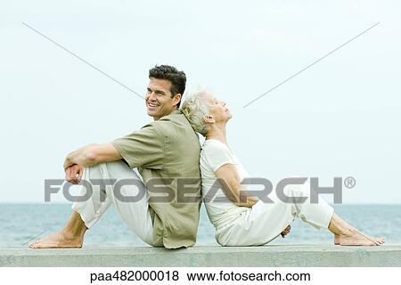 Senior woman and adult son sitting back to back by the sea, side view View Large Photo Image Stock Photo - Senior woman and adult son sitting back to back by the sea, side view. Fotosearch