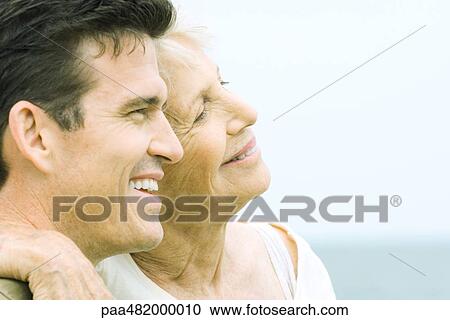 Stock Image - Senior woman and adult son smiling together, cheek to cheek, side view. Fotosearch