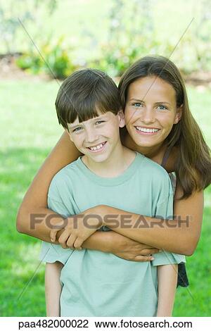 Stock Image - Teenage girl and younger brother smiling at camera together, portrait. Fotosearch