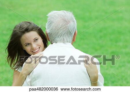 Stock Photograph - Teenage girl hugging her grandfather outdoors, smiling. Fotosearch