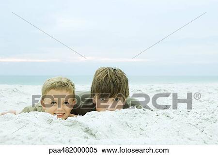 Stock Photography - Two brothers lying on the beach together, both smiling at camera, portrait. Fotosearch