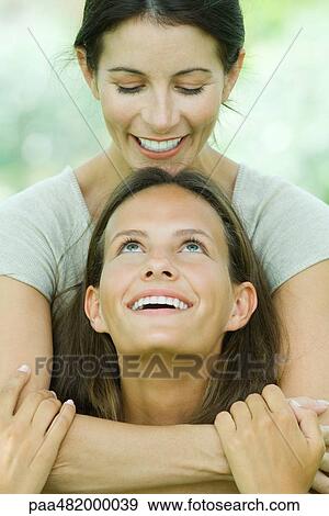 Woman embracing teen daughter from behind, both smiling at each other View Large Photo Image Stock Photo - Woman embracing teen daughter from behind, both smiling at each other. Fotosearch