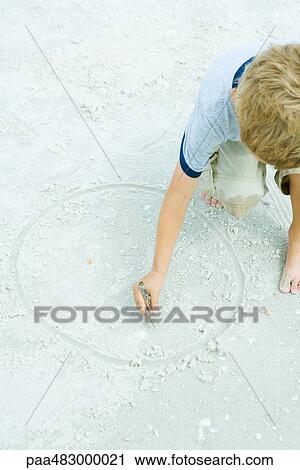 Stock Image - Child drawing circle in the sand with a stick, cropped view. Fotosearch