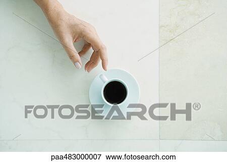 Stock Photo - Hand reaching for coffee cup, viewed from directly above. Fotosearch