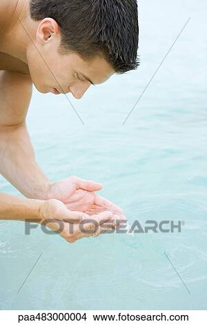 Man bending over, holding water in cupped hands, cropped view View Large Photo Image Picture - Man bending over, holding water in cupped hands, cropped view. Fotosearch