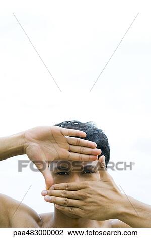 Stock Image - Man looking at camera through finger frame, close-up. Fotosearch