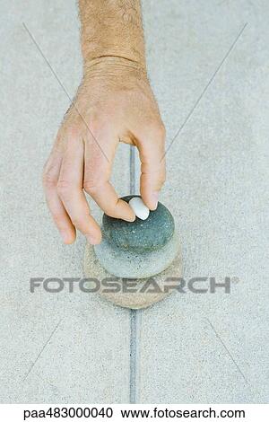 Stock Image - Man stacking pebbles, cropped view of hand. Fotosearch