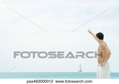 Man standing in front of sea, waving at sailboat in distance View Large Photo Image Stock Image - Man standing in front of sea, waving at sailboat in distance. Fotosearch