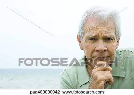 Senior man furrowing brow, hand under chin, looking at camera View Large Photo Image Stock Image - Senior man furrowing brow, hand under chin, looking at camera. Fotosearch