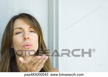 Stock Image - Woman blowing kiss at camera, close-up. Fotosearch