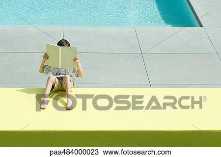 Boy reading beside swimming pool, face obscured by book, high angle view View Large Photo Image Stock Image - Boy reading beside swimming pool, face obscured by book, high angle view. Fotosearch