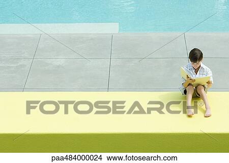 Boy sitting by swimming pool, reading book View Large Photo Image Picture - Boy sitting by swimming pool, reading book. Fotosearch