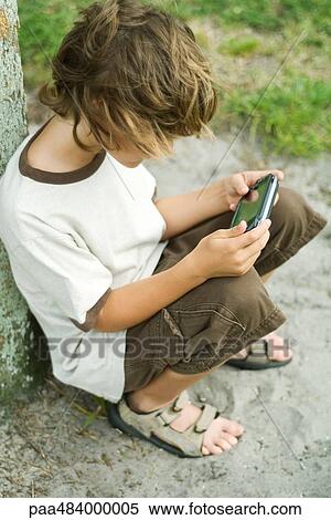 Boy sitting on the ground playing with handheld video game, high angle view View Large Photo Image Stock Photography - Boy sitting on the ground playing with handheld video game, high angle view. Fotosearch