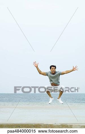 Man jumping in the air at the beach, arms out, looking at camera View Large Photo Image Stock Photography - Man jumping in the air at the beach, arms out, looking at camera. Fotosearch