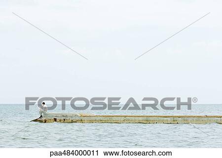 Man sitting at the end of pier, reading book, in the distance View Large Photo Image Stock Image - Man sitting at the end of pier, reading book, in the distance. Fotosearch