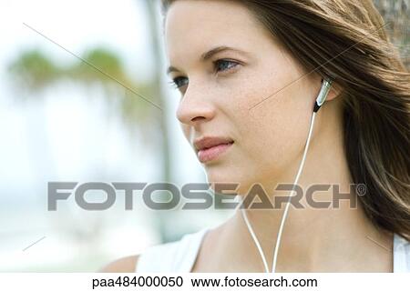 Stock Image - Teenage girl listening to headphones, looking away, close-up. Fotosearch