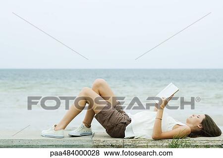 Teenage girl lying on the ground with knees up, reading book, side view View Large Photo Image Stock Photo - Teenage girl lying on the ground with knees up, reading book, side view. Fotosearch