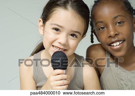Two little girls smiling at camera together, one holding up microphone View Large Photo Image Stock Image - Two little girls smiling at camera together, one holding up microphone. Fotosearch