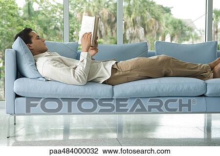 Young man lying on couch reading book, side view View Large Photo Image Stock Image - Young man lying on couch reading book, side view. Fotosearch