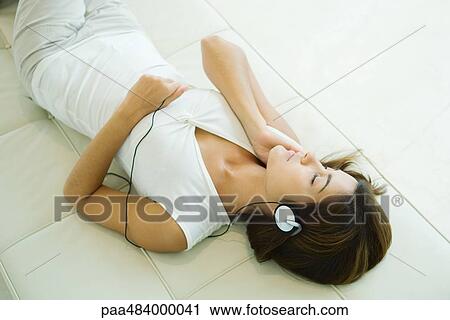 Young woman lying on back listening to headphones, eyes closed View Large Photo Image Stock Image - Young woman lying on back listening to headphones, eyes closed. Fotosearch