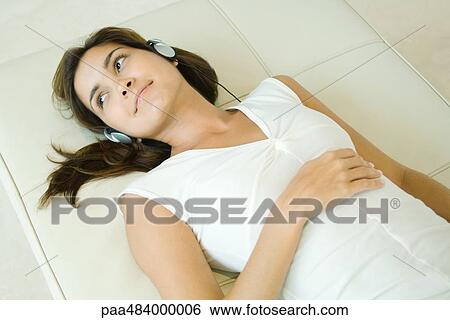 Young woman lying on back listening to headphones, smiling, high angle view View Large Photo Image Stock Photograph - Young woman lying on back listening to headphones, smiling, high angle view. Fotosearch