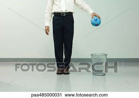 Businessman holding globe over trash can, chest down, front view View Large Photo Image Stock Image - Businessman holding globe over trash can, chest down, front view. Fotosearch