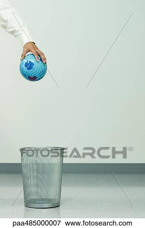 Stock Photo - Businessman holding globe over trash can, cropped. Fotosearch
