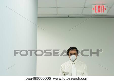 Businessman wearing pollution mask, under exit sign, looking at camera View Large Photo Image Stock Photography - Businessman wearing pollution mask, under exit sign, looking at camera. Fotosearch