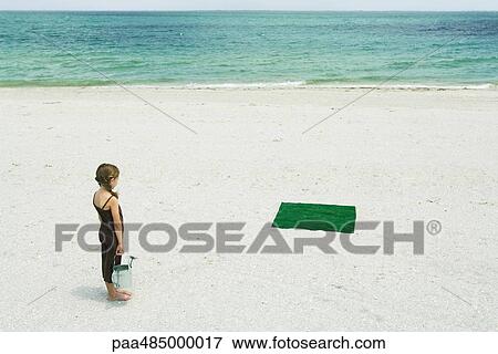 Girl standing on beach, facing square of artificial turf, holding watering can, high angle view View Large Photo Image Stock Photo - Girl standing on beach, facing square of artificial turf, holding watering can, high angle view. Fotosearch