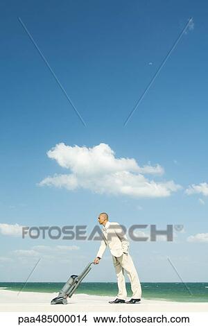 Man in suit using vacuum cleaner on beach, full length View Large Photo Image Picture - Man in suit using vacuum cleaner on beach, full length. Fotosearch