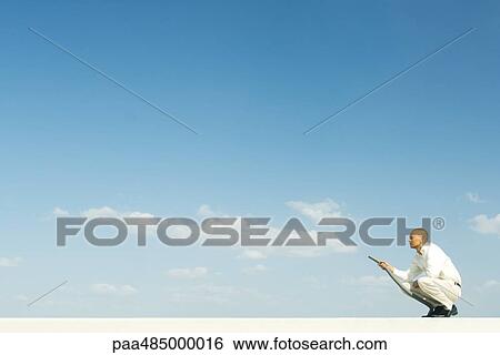 Stock Photograph - Man vacuuming clouds, full length. Fotosearch