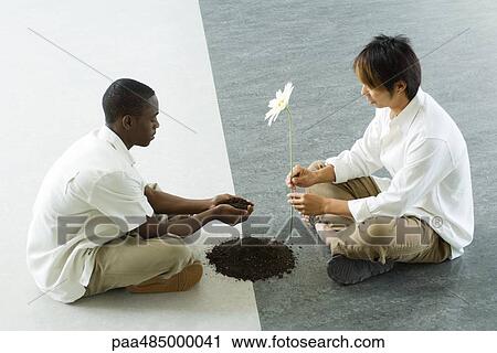 Two males sitting face to face on ground, one holding out handful of soil, the other holding out a flower View Large Photo Image Stock Image - Two males sitting face to face on ground, one holding out handful of soil, the other holding out a flower. Fotosearch