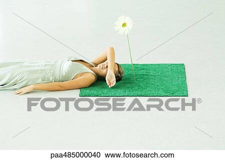 Woman lying with head on square of artificial turf, covering eyes with arm View Large Photo Image Stock Image - Woman lying with head on square of artificial turf, covering eyes with arm. Fotosearch