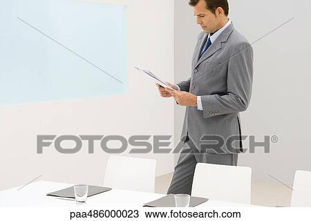 Stock Image - Business executive standing in office, reading report. Fotosearch