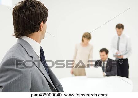 Businessman looking over shoulder at associates in background, close-up View Large Photo Image Stock Image - Businessman looking over shoulder at associates in background, close-up. Fotosearch