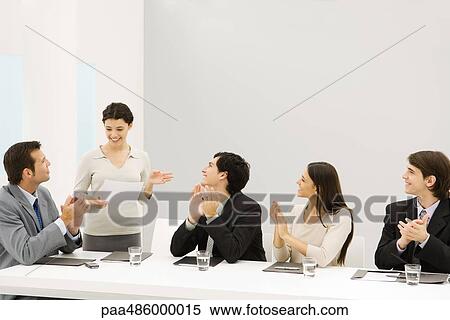 Stock Photography - Businesswoman standing and speaking, seated colleagues clapping, smiling. Fotosearch