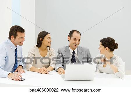 Stock Image - Group of male and female business partners sitting together at table with laptop computer, smiling. Fotosearch