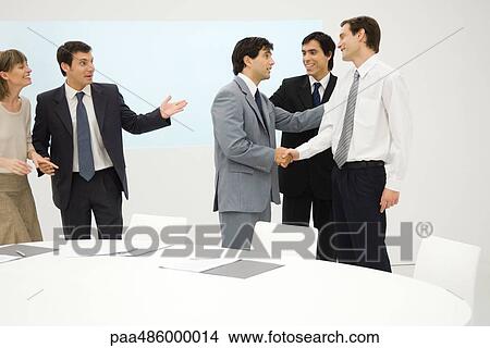 Group of professionals standing beside table, smiling, two shaking hands View Large Photo Image Picture - Group of professionals standing beside table, smiling, two shaking hands. Fotosearch