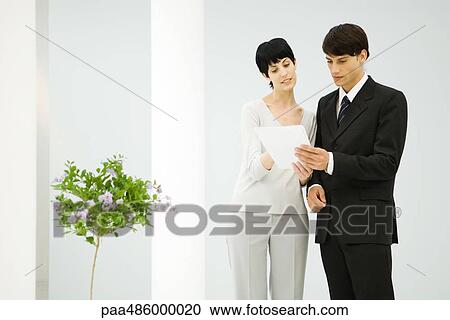 Male and female business partners standing side by side, discussing document View Large Photo Image Stock Image - Male and female business partners standing side by side, discussing document. Fotosearch